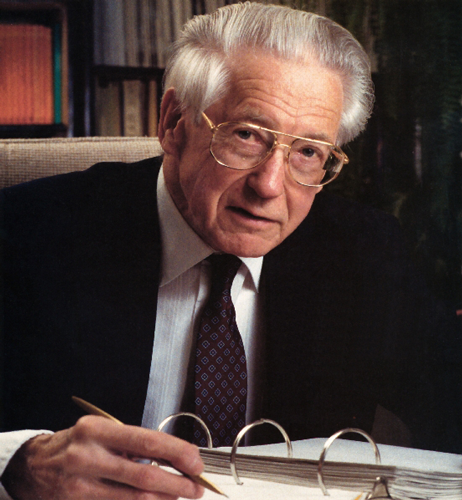 A man in a suit looks up from his notebook at the camera
